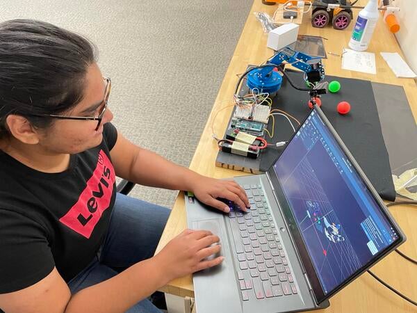 Student typing on laptop in robotics lab